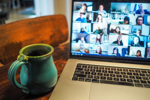Photo of a table set up with a coffee mug on the left and a laptop on the right that shows a video conference on screen