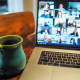 Photo of a table set up with a coffee mug on the left and a laptop on the right that shows a video conference on screen