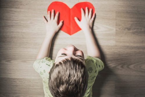 Little blond child on his hand on a red paper heart